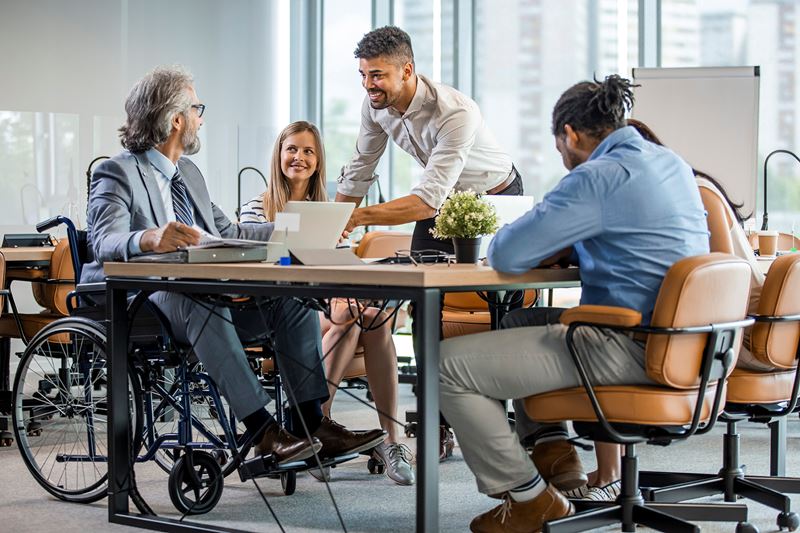 A diverse group of people working in a bright office. One man is in a wheelchair.